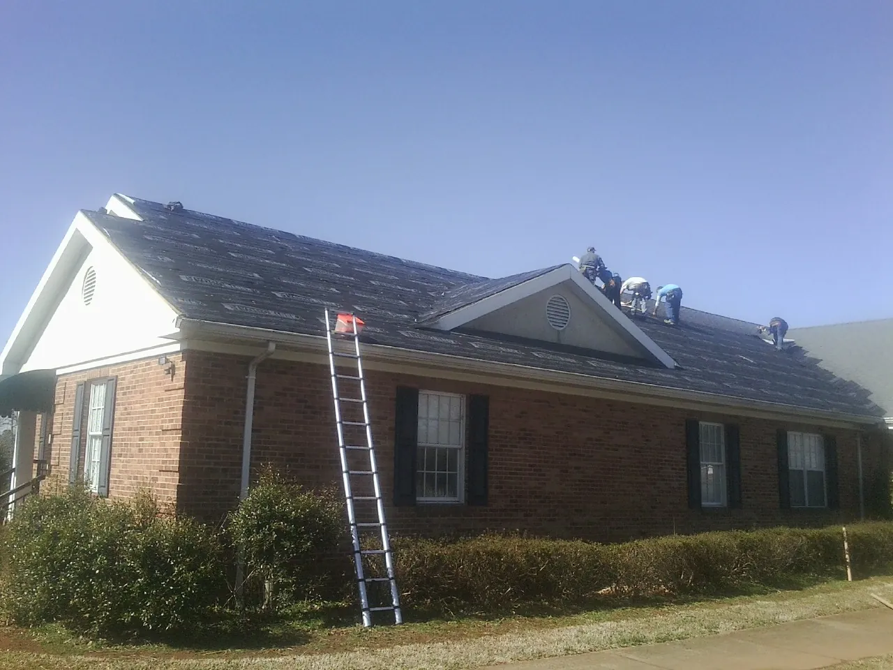Crew tearing shingles off a brick ranch roof with a ladder set — Emergency Roof Repair work by our crew in White Swan