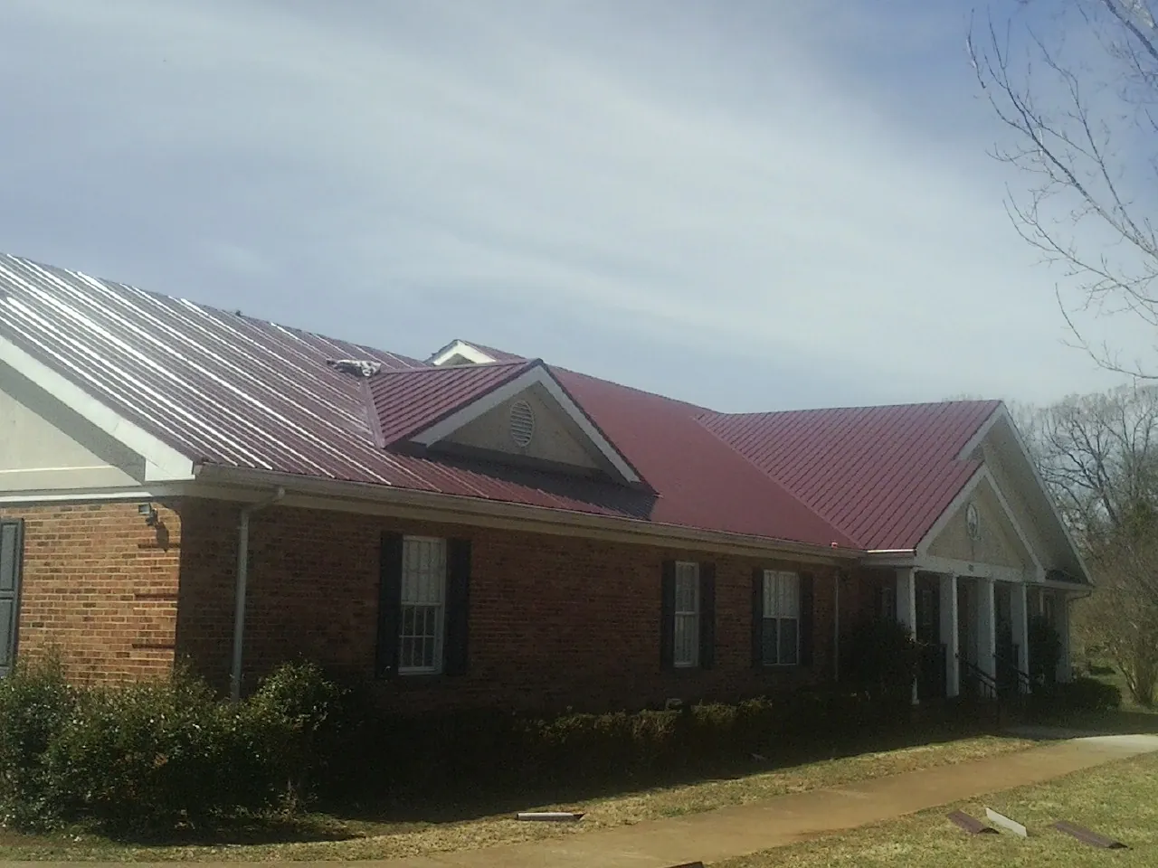 Red metal roof with gabled entries on a long brick building, from a Hail Damage Roof Repair job in White Swan