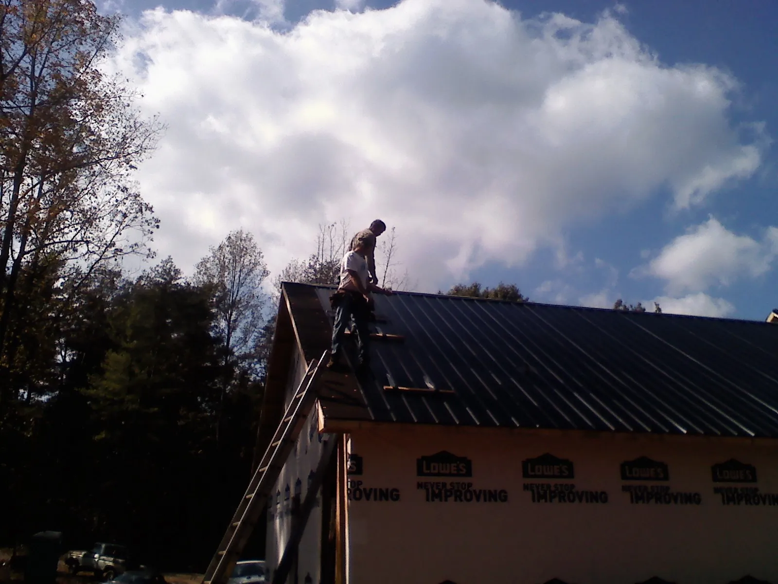 Roofer fastening dark metal panels high against a cloudy sky, from a Roof Inspection job in White Swan