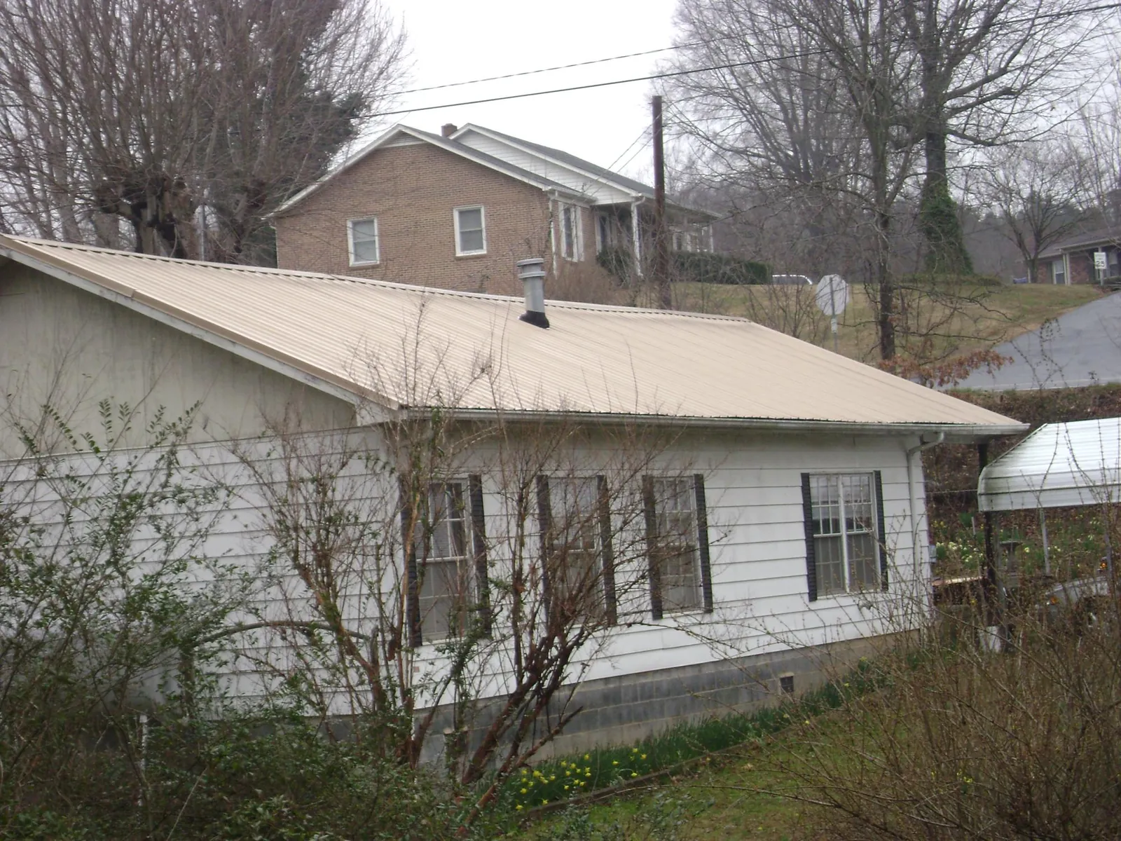 Tan metal roof on a white sided house set into a hillside — Commercial Roofing by Roofing Brothers in White Swan
